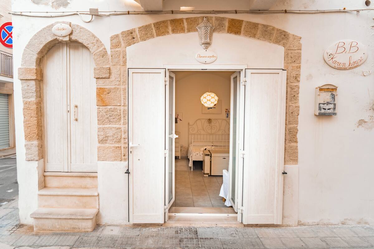 A hotel entrance with a stone archway, a sign reading 'BeB Karen House,' and a street sign indicating no parking.