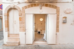 Entrada de um hotel com um arco de pedra, uma placa com o texto 'BeB Karen House' e uma placa de rua indicando proibido estacionar.