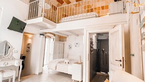 Ein geräumiges Zimmer mit hohen Decken, einem Balkon, einem Bett, einem Schreibtisch und einem Badezimmer.
