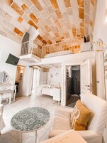 Um quarto amplo com teto alto, varanda, cama, escrivaninha e banheiro.