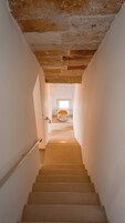 Escada que leva a um quarto com janela, uma porta branca e vista para outra janela acima.