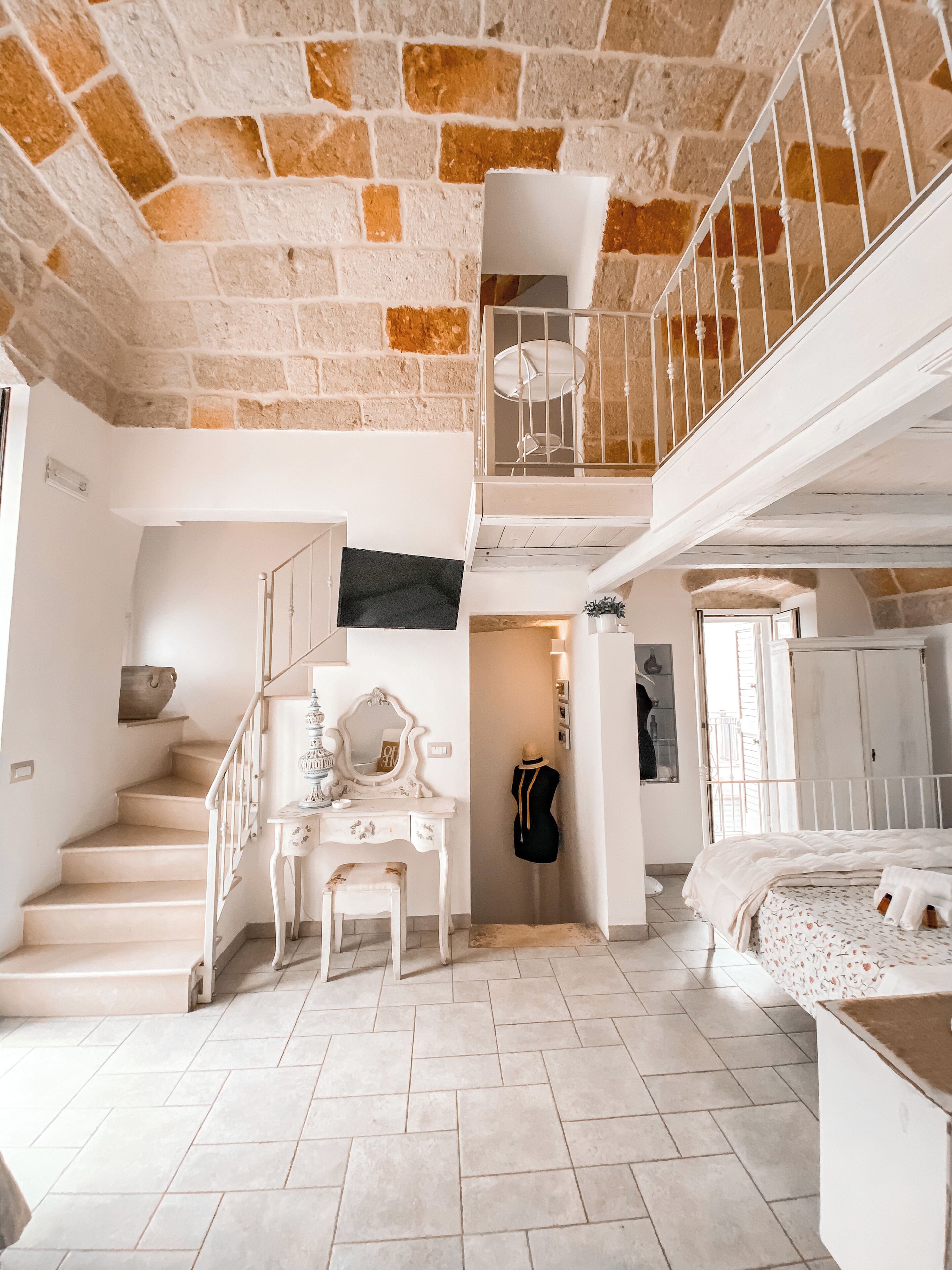 A spacious room with a staircase, a vanity with a mirror, and a bed with a patterned bedspread.