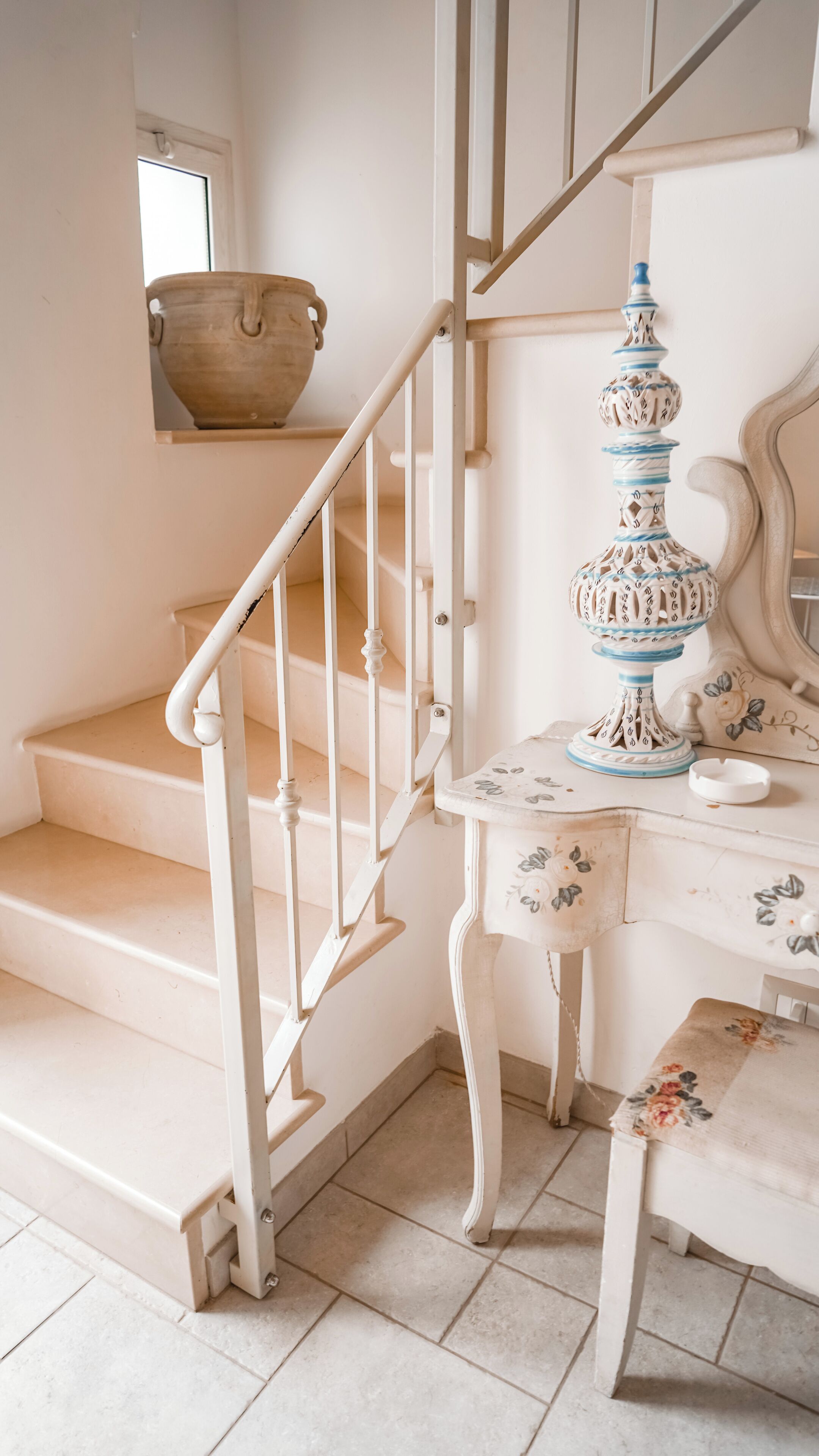 A staircase with white railings, a small table with a floral tablecloth, and a decorative vase.