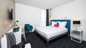 Ein modernes Hotelzimmer mit Bett, Schreibtisch, Sessel, Fernseher und Lampe.