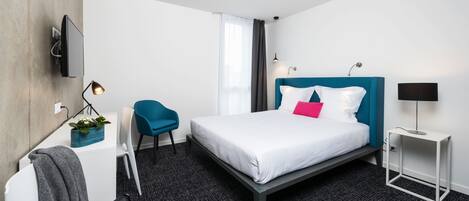 Una habitación de hotel moderna con una cama, un escritorio, una silla, un televisor y una lámpara.