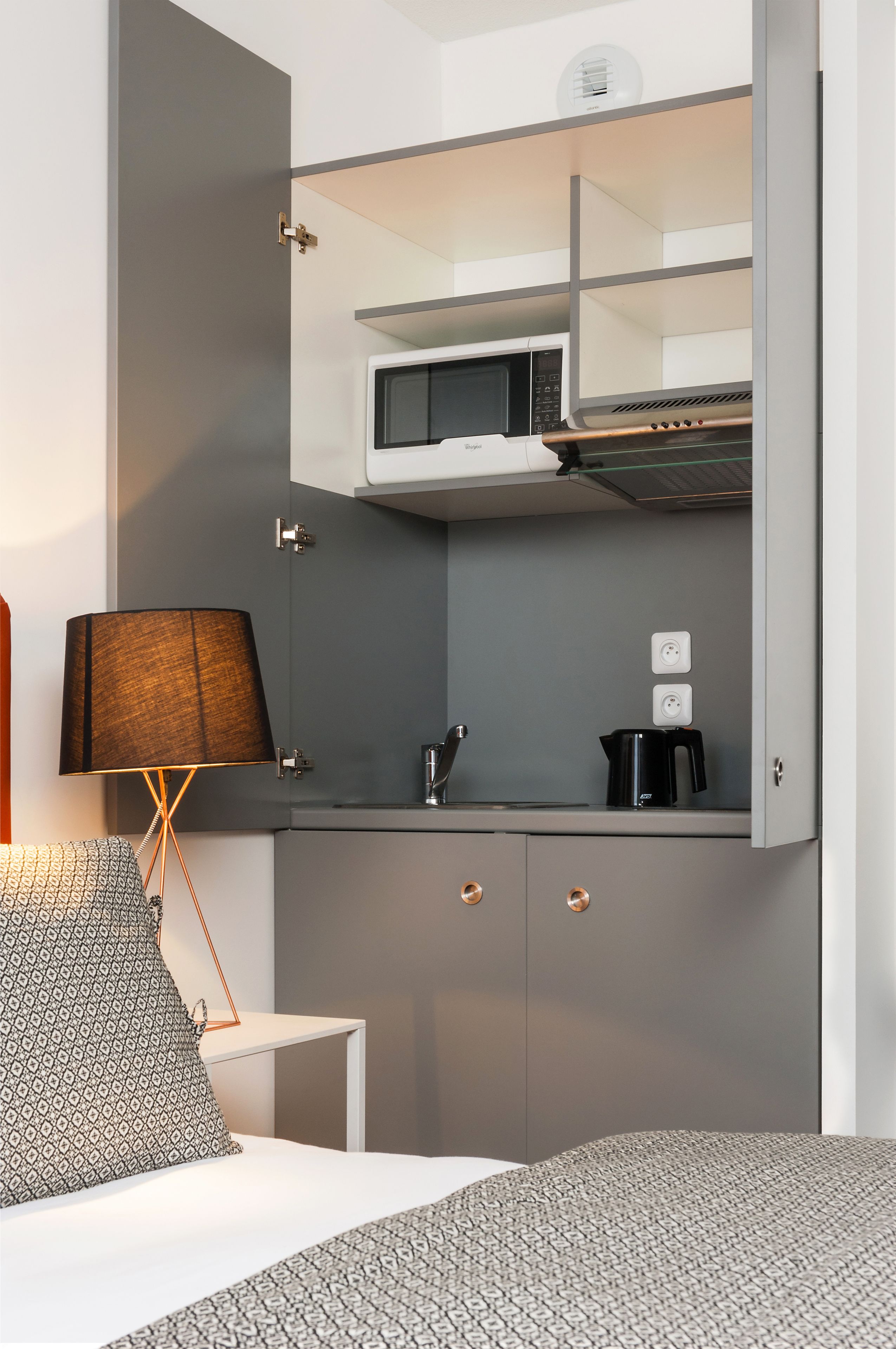 Una kitchenette compacta con microondas, cafetera y una pequeña encimera.
