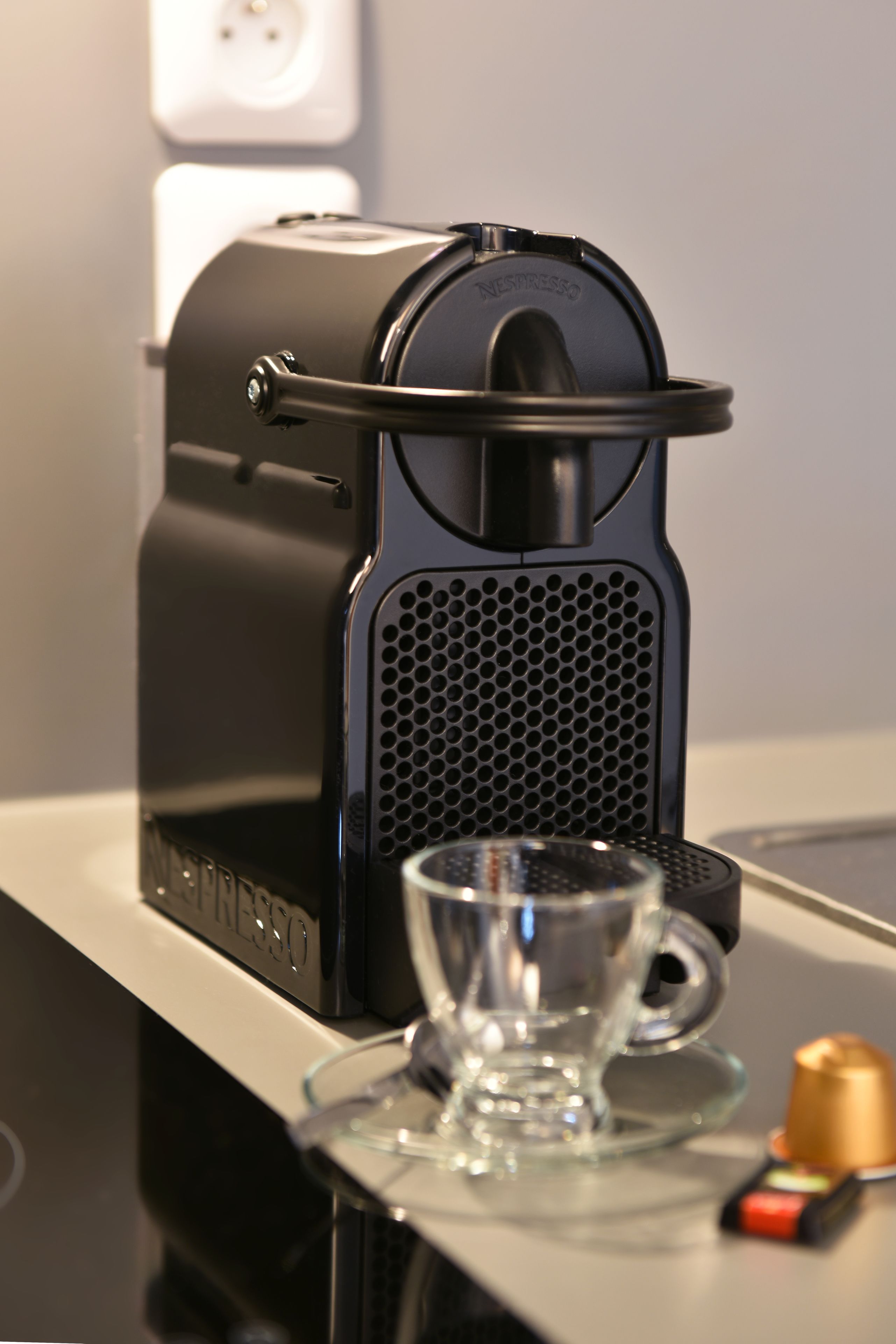 Eine Kaffeemaschine auf einer Arbeitsplatte, neben ihr eine Tasse und ein kleiner Behälter.