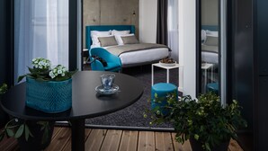 A modern hotel room with a bed, a small table with a plant, and a view of the room through a glass door.