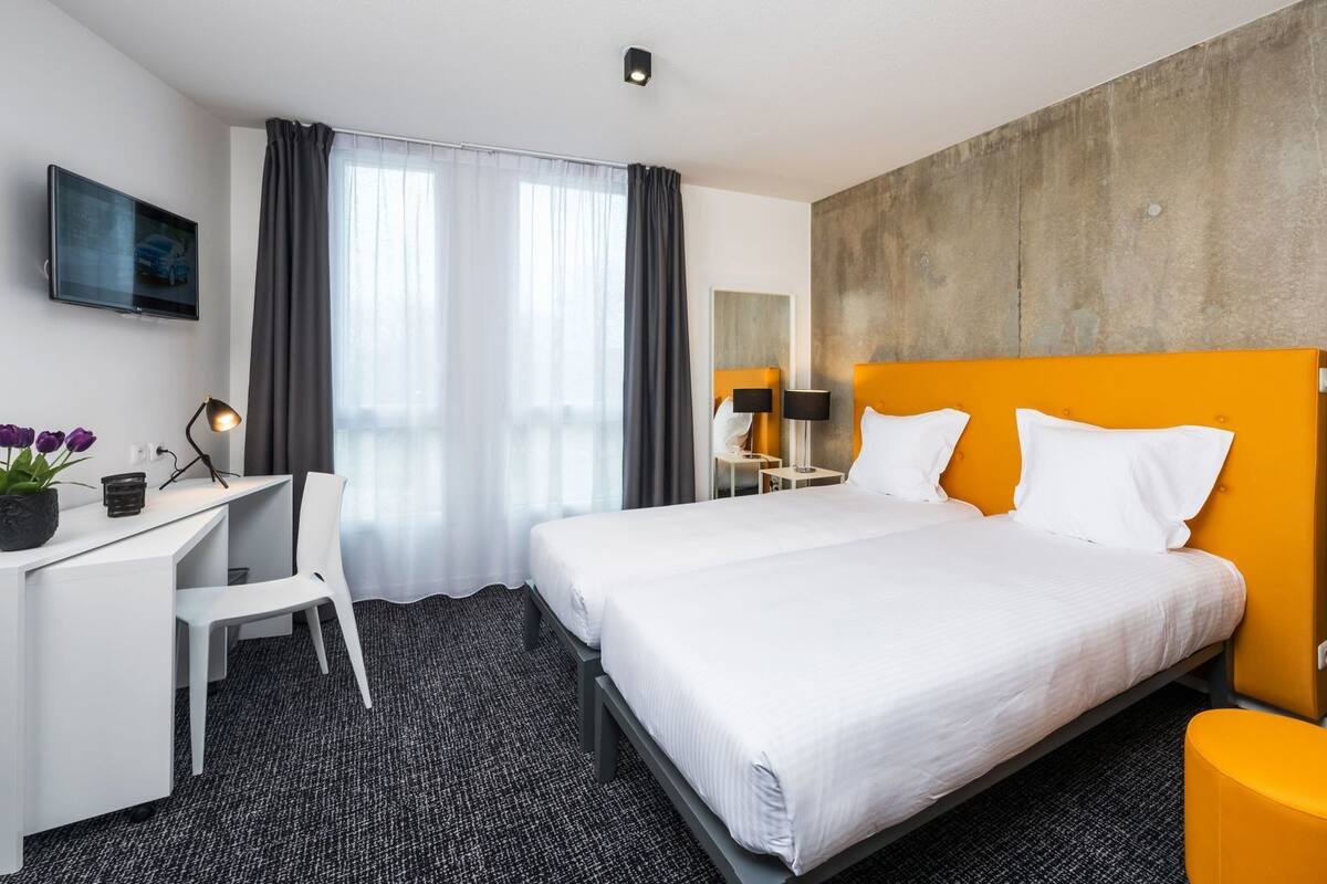A hotel room with a bed, a desk, a chair, a TV, and a large window with curtains.