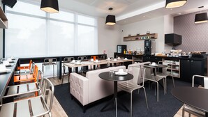 A modern dining area with tables and chairs, a kitchen area with appliances, and a large window providing natural light.