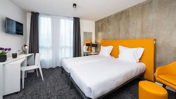 Une chambre d’hôtel avec un lit, un bureau, une chaise, une télévision et une fenêtre avec des rideaux.