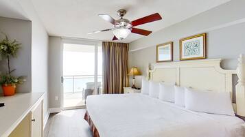 A hotel room with a large bed, a ceiling fan, a balcony with curtains, and two framed pictures on the wall.