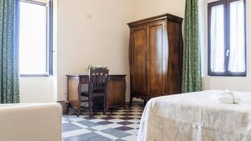 A room with a checkered floor, a bed with a white bedspread, a wooden desk with a chair, and a wardrobe.