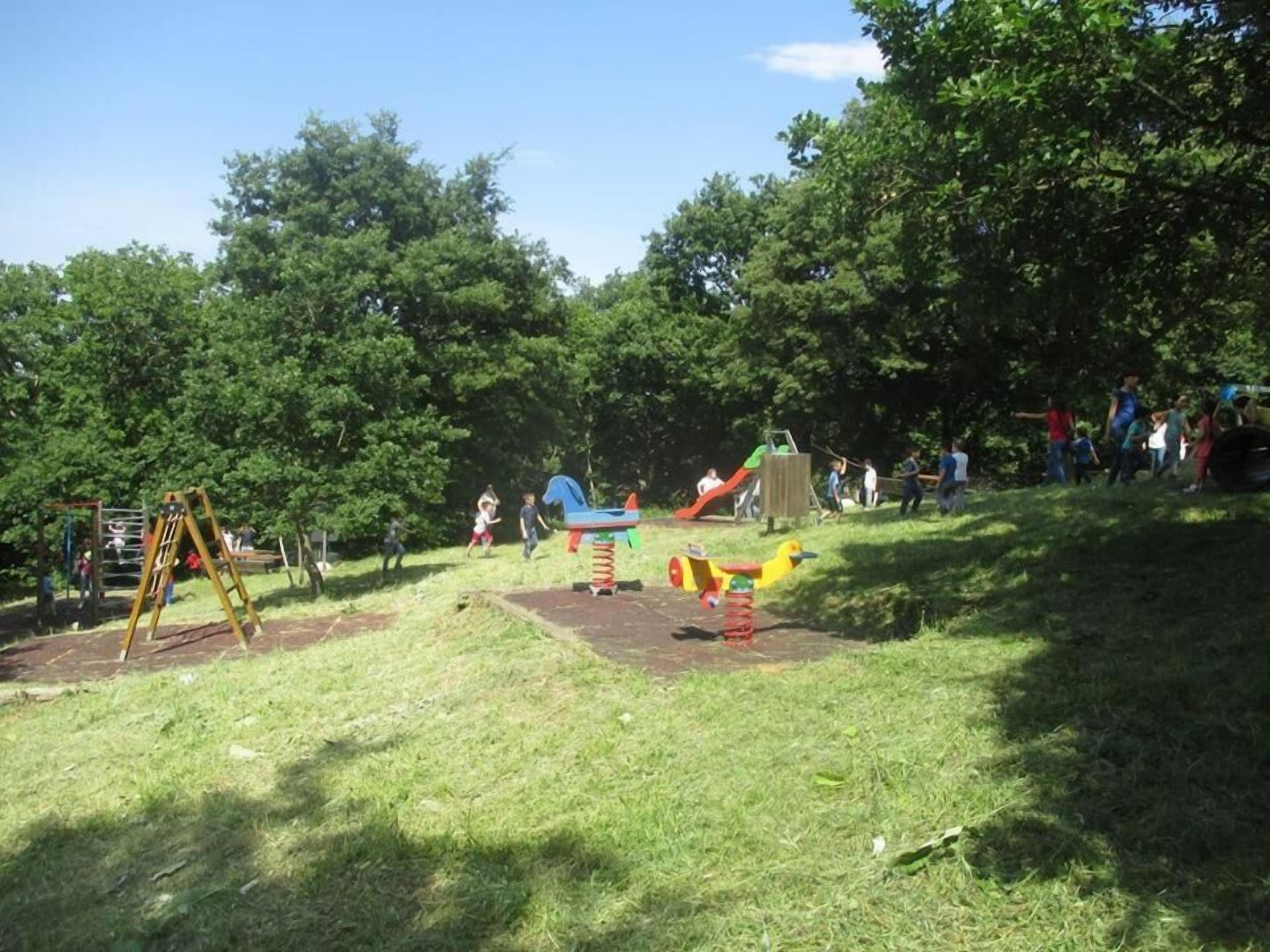 A playground with various play structures, surrounded by trees and grassy areas.