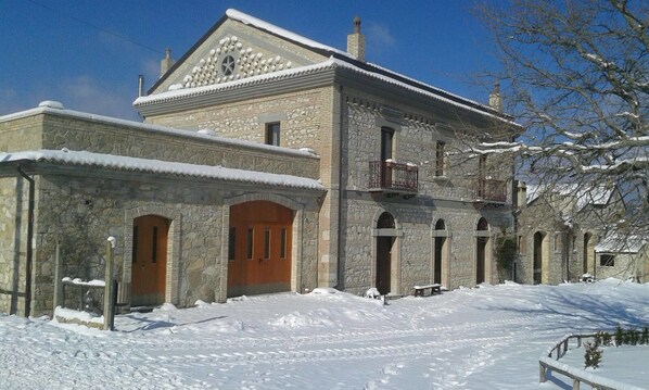 A stone building with a wooden door and arched windows, surrounded by snow. - Masseria Salecchia (Bovino)