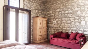 Une pièce avec un mur en pierre, une armoire en bois, un canapé rouge et un lit avec une literie à motifs.