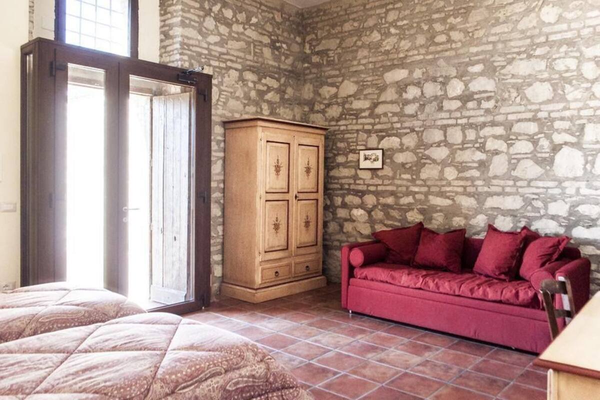 A room with a stone wall, a wooden cabinet, a red sofa, and a bed with patterned bedding.