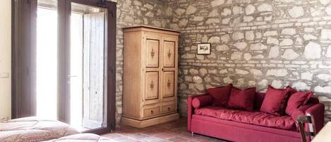 A room with a stone wall, a wooden cabinet, a red sofa, and a bed with patterned bedding.