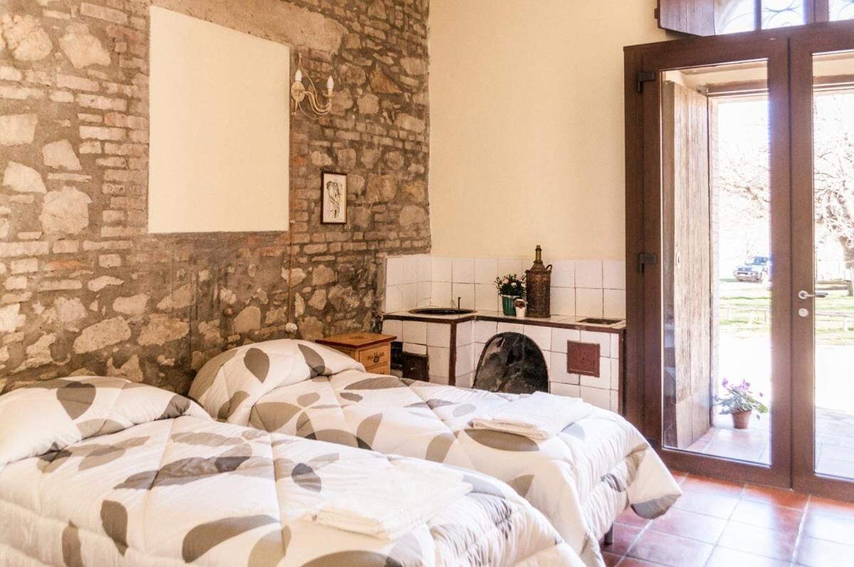 Une chambre avec deux lits, un mur en pierre, un petit coin cuisine et une porte donnant sur un espace extérieur.