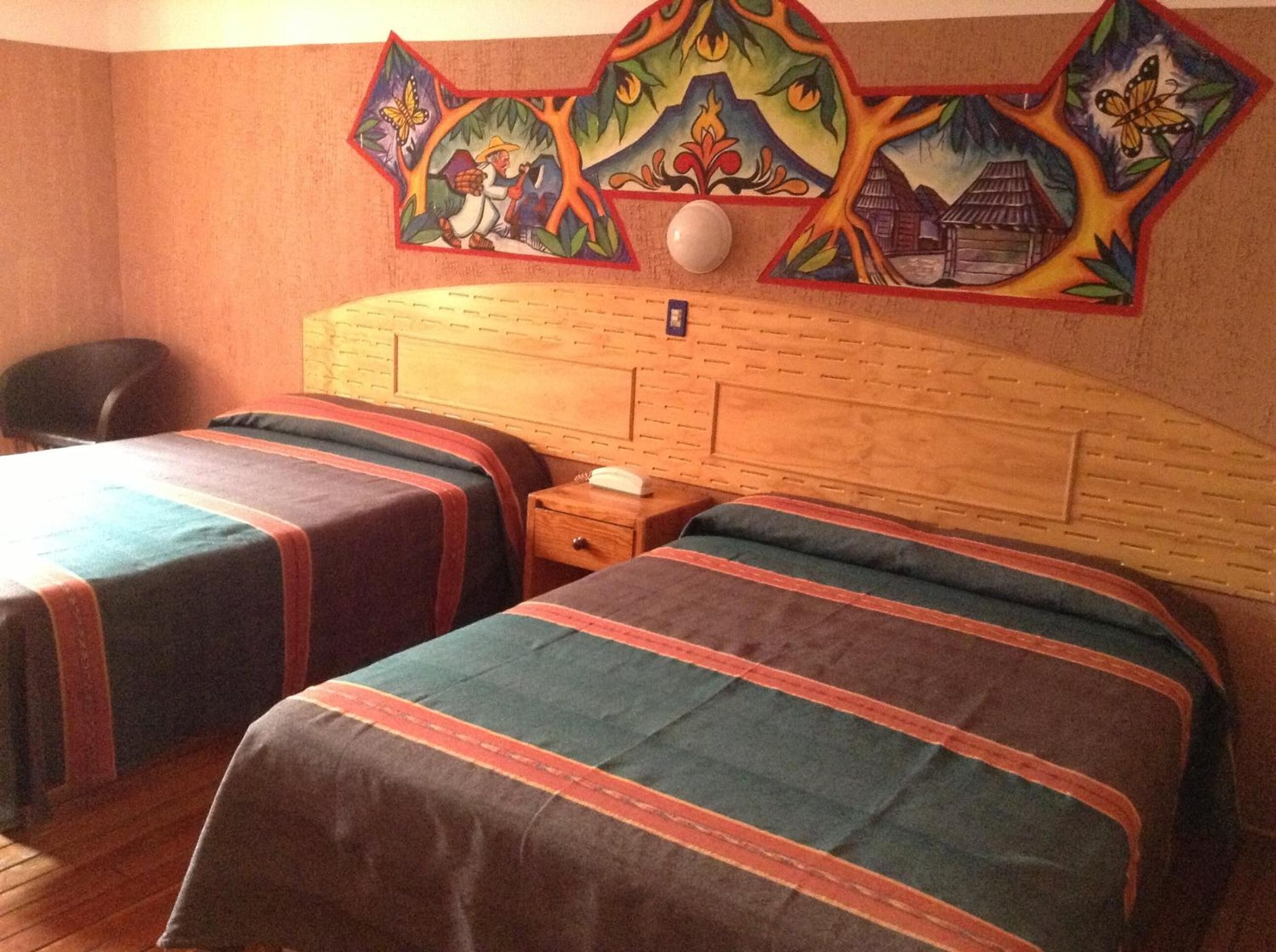 A hotel room with two beds, a wooden headboard, a nightstand, and a wall mural.