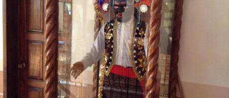 Un maniquí en una vitrina de vidrio con tocado ornamental, camisa blanca y falda roja.