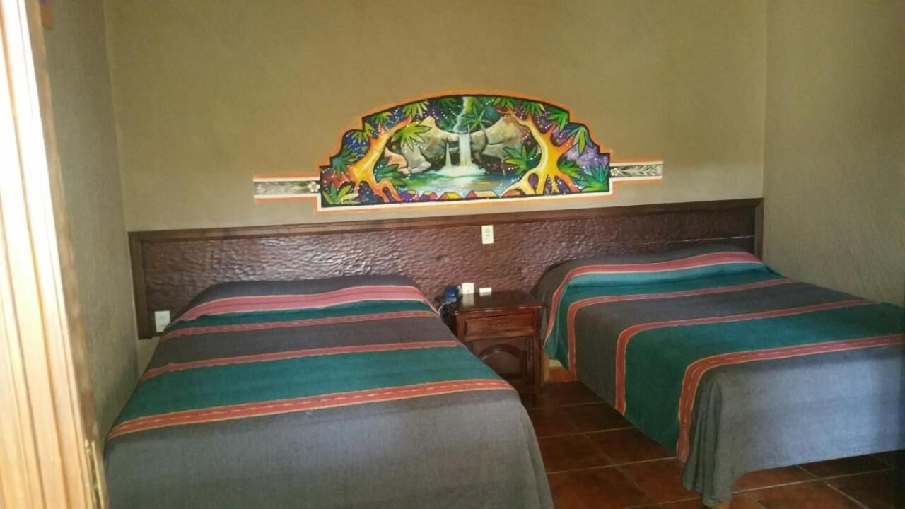 Habitación con dos camas, cada una con ropa de cama a rayas, un mural en la pared y cabeceros de madera.