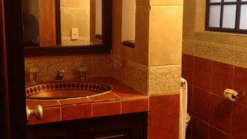 Un baño con un mueble de madera oscura, un lavabo y un espejo. Hay un perchero en la pared y una ventana con diseño de cuadrícula.