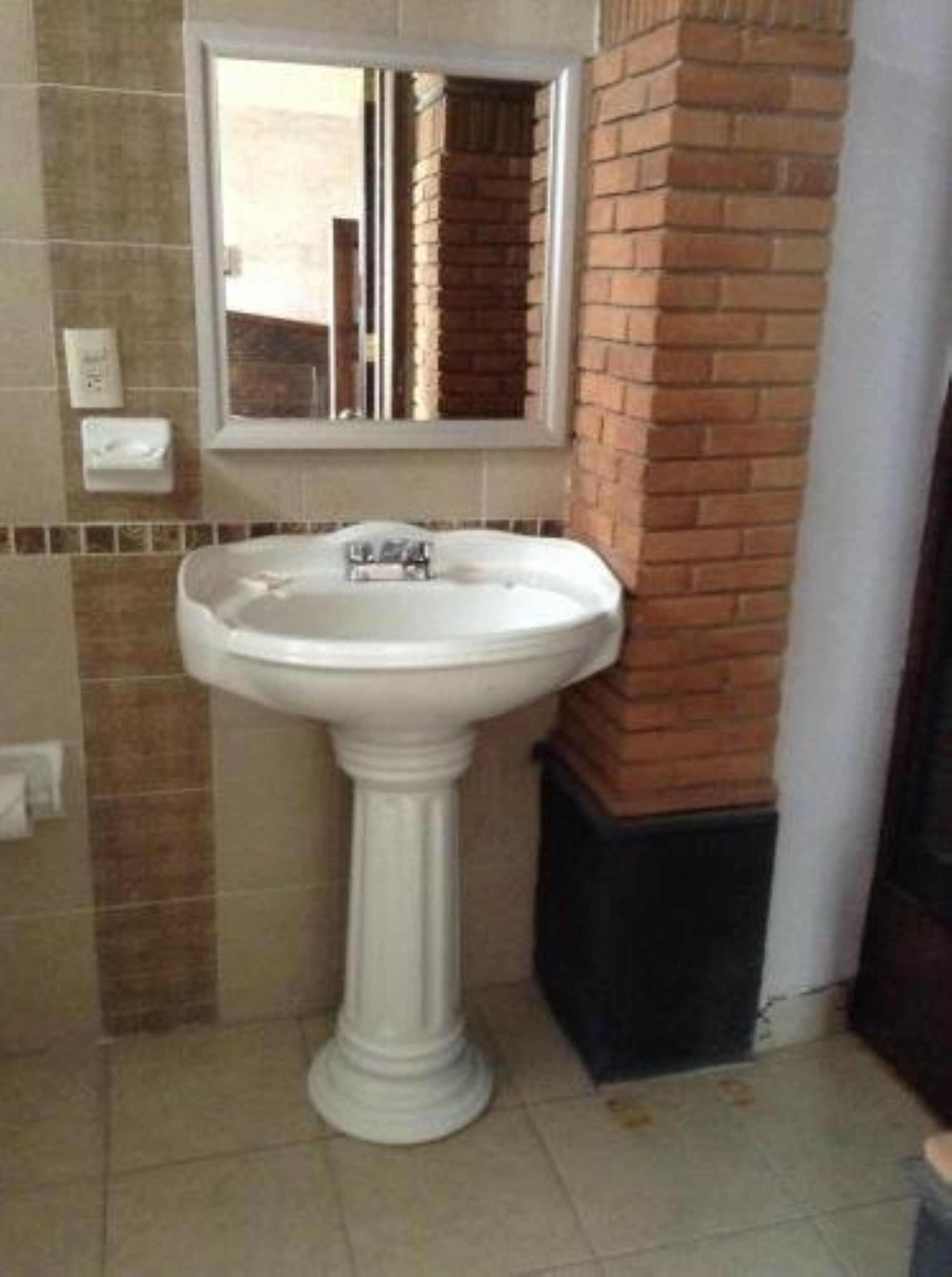 Un baño con lavamanos pedestal, un espejo encima y suelo de baldosas.