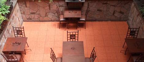 Un patio con una mesa y sillas en el centro, rodeado de plantas en macetas y una fuente decorativa.