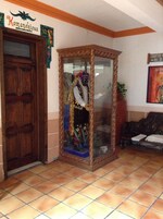 A room with a wooden door, a glass display case with a statue, a sign reading "Komanchicua", and a poster on the wall.