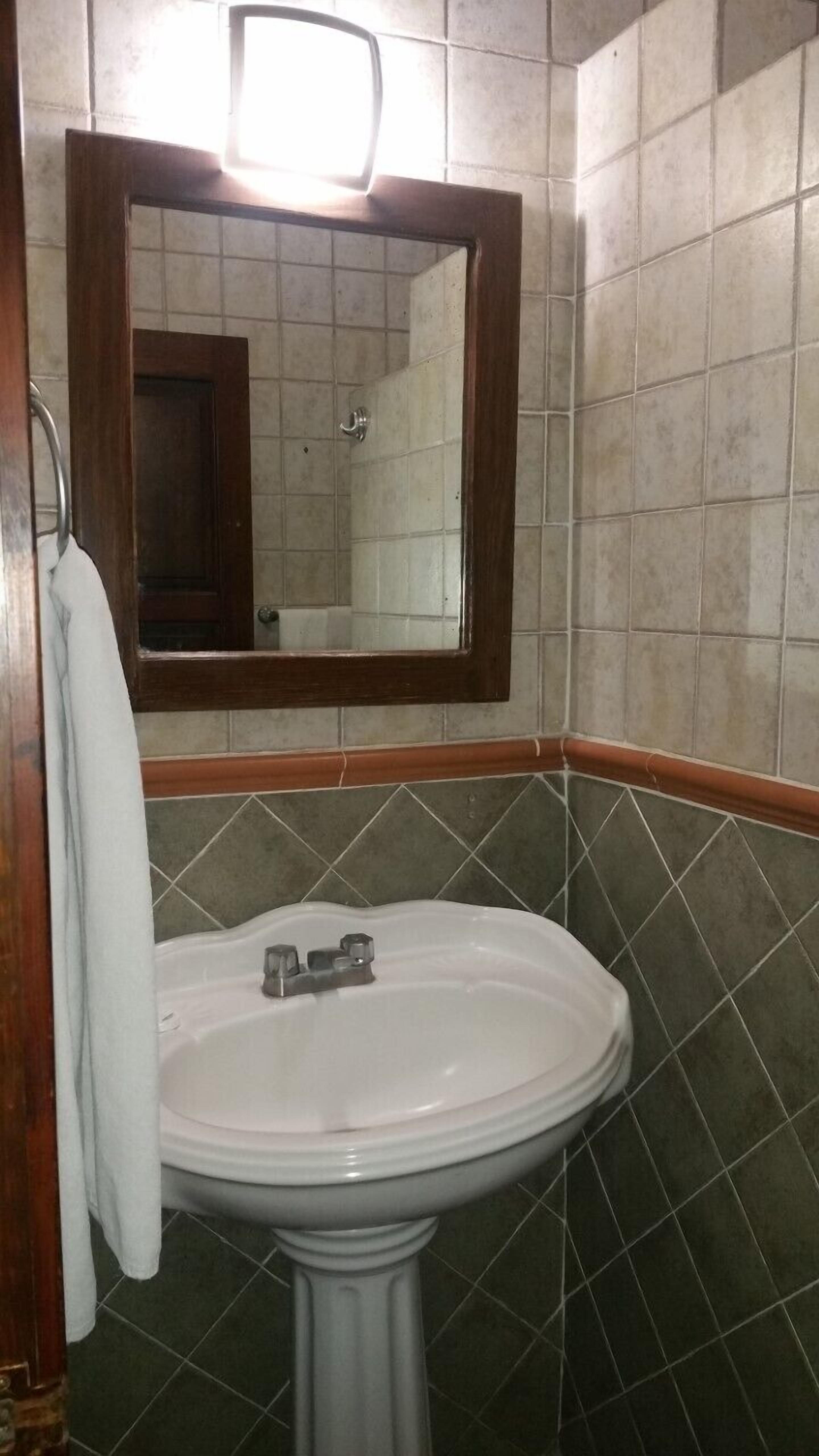 A bathroom with a pedestal sink, a mirror with a wooden frame, and tiled walls.