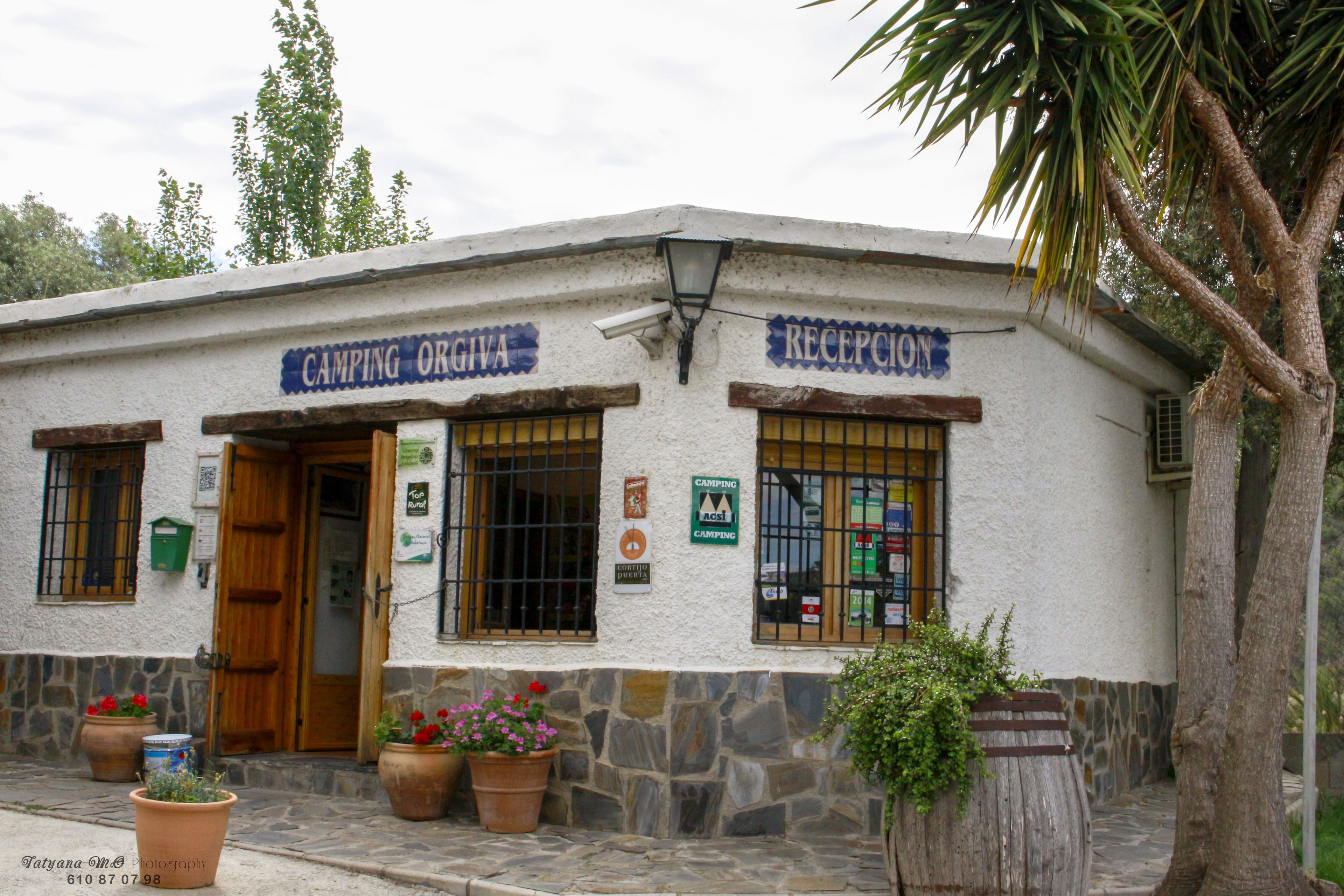 Ein Gebäude mit Schildern "CAMPING ORGA" und "RECEPTION", Steinmauern, Holztüren und Topfpflanzen.