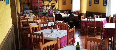 A restaurant with wooden tables and chairs, yellow walls, and a chandelier.