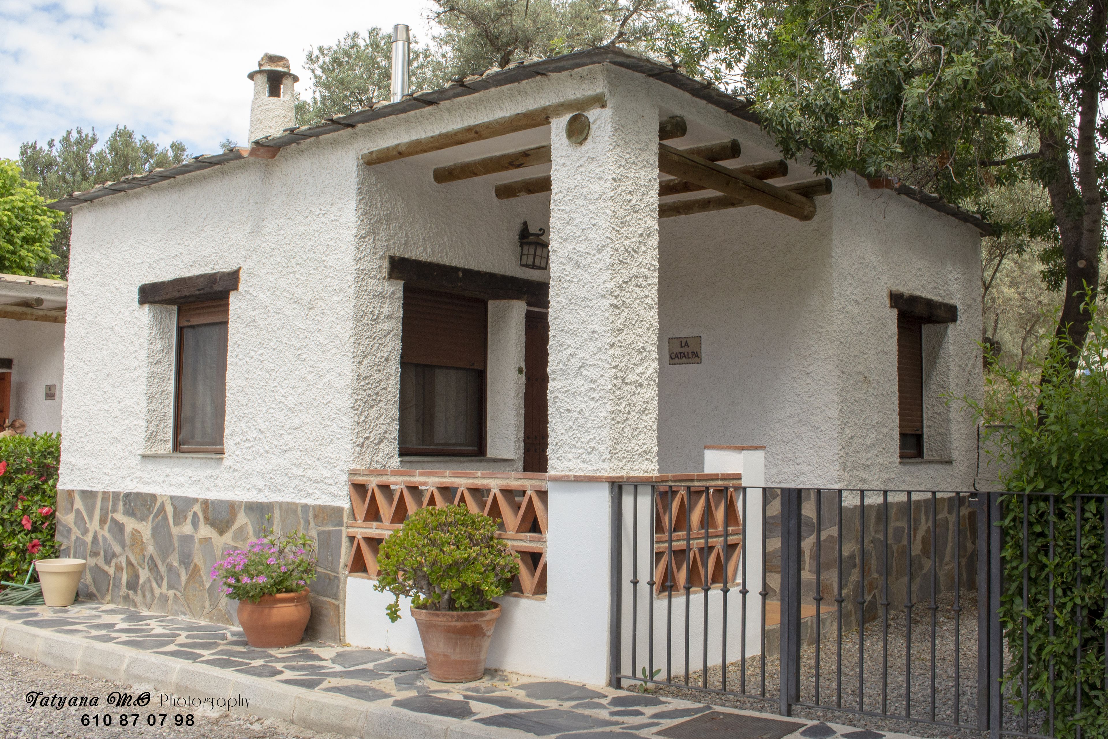 A small, white building with a stone base, wooden beams, and a metal fence.