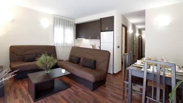 Un salon moderne avec un canapé marron, une table basse et un coin repas avec une table dressée pour deux personnes.