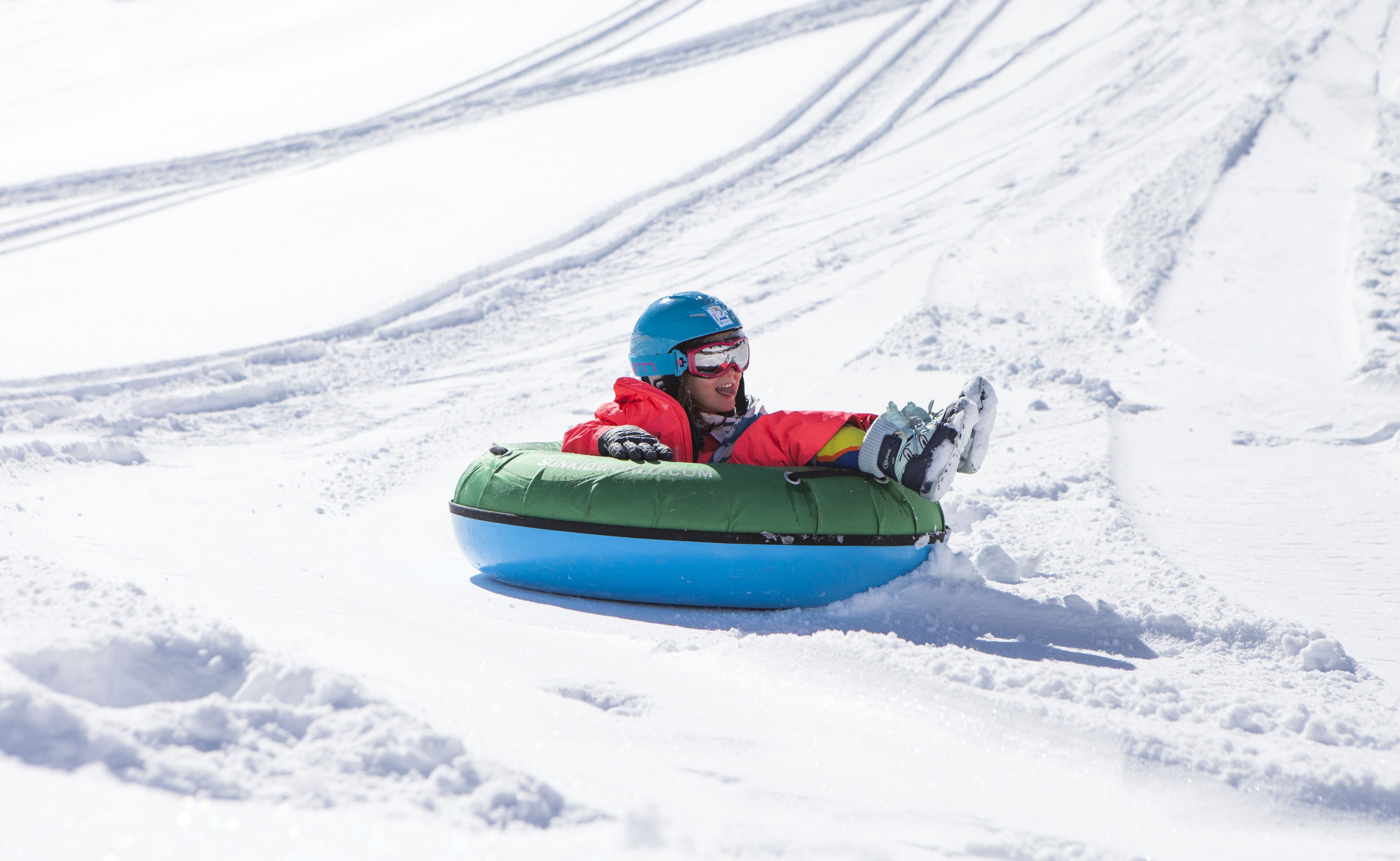A person in a red jacket and blue helmet sitting in a blue snow tube on a snowy slope.