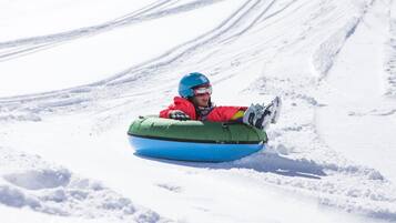 A person in a red jacket and blue helmet sitting in a blue snow tube on a snowy slope.