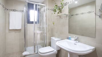 A modern bathroom with a glass shower enclosure, a white toilet, and a sink with a mirror above it.