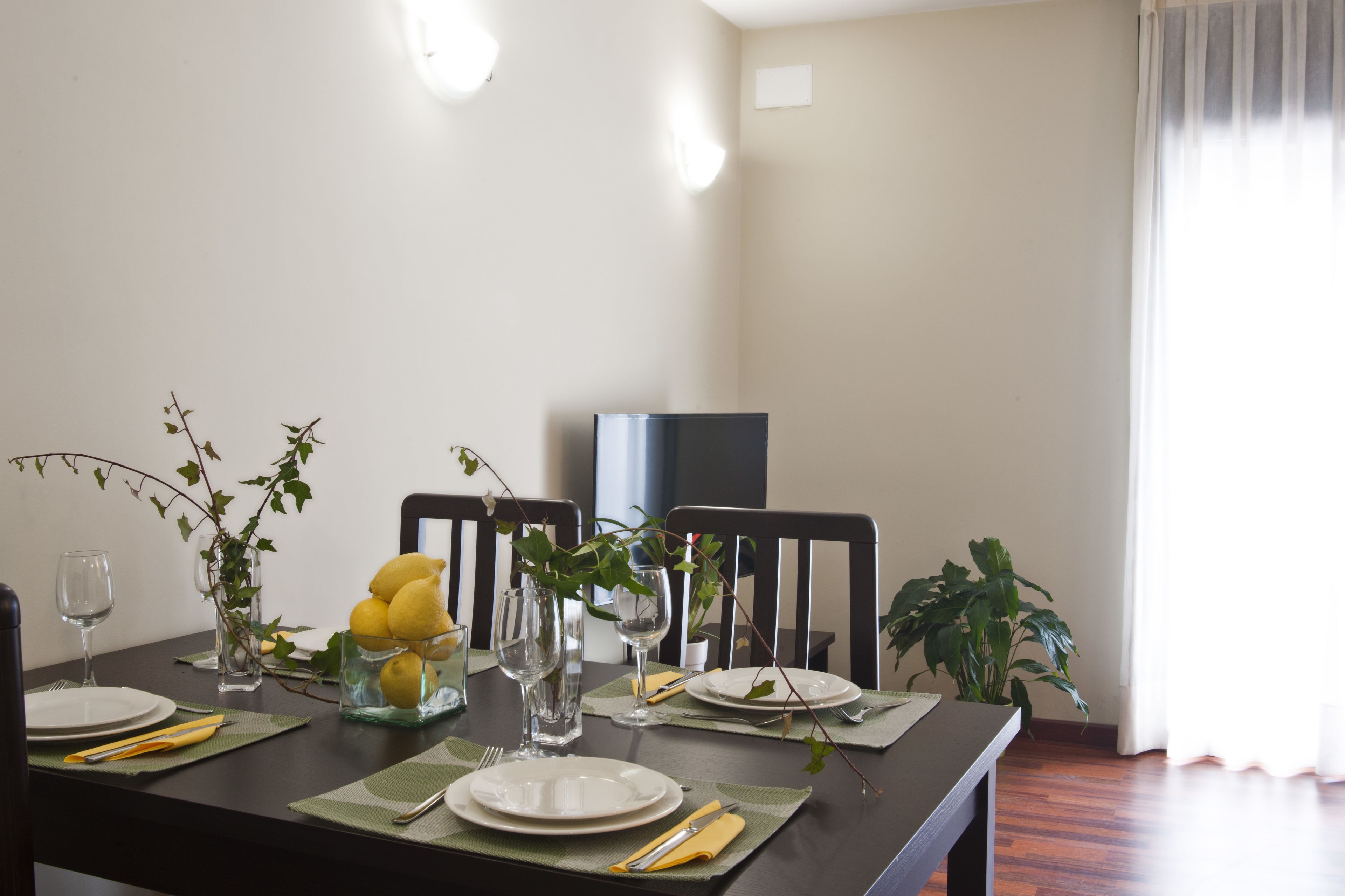 Una mesa de comedor lista con platos, cubiertos y un florero con limones.