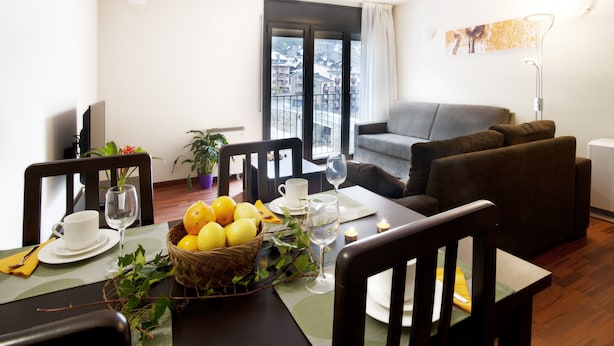 A dining area with a table set for two, a basket of lemons, a potted plant, and a view of the city through a balcony door. - Andorra4days Soldeu - El Tarter (Soldeu)