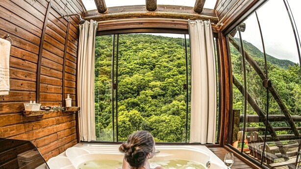 A person relaxing in a wooden bathtub with a view of a forested hillside. - Cachoeira dos Borges Cabanas e Parque (Mampituba)