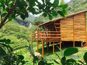 A wooden cabin with a wooden deck, surrounded by lush greenery and a mountainous backdrop. - Cachoeira dos Borges Cabanas e Parque (Mampituba)
