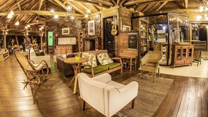 A rustic interior with wooden beams, a stone wall, a fireplace, and a variety of seating options including a sofa, chairs, and a dining table. - Cachoeira dos Borges Cabanas e Parque (Mampituba)