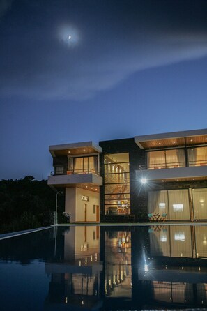 A modern two-story house with a balcony, large windows, and a swimming pool reflecting the building. - Lodge Natur Zen (Ponta Delgada)