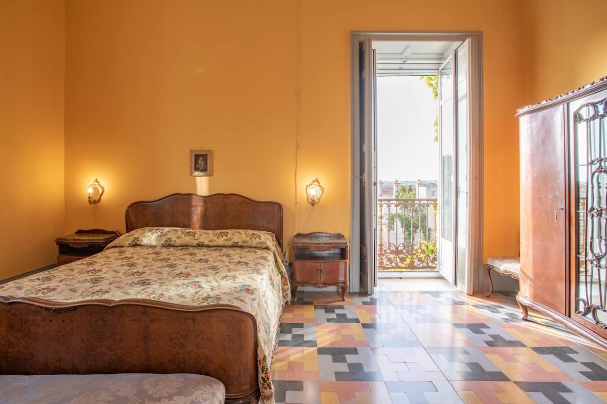 Quarto com cama, mesas de cabeceira, guarda-roupa e varanda com grade.