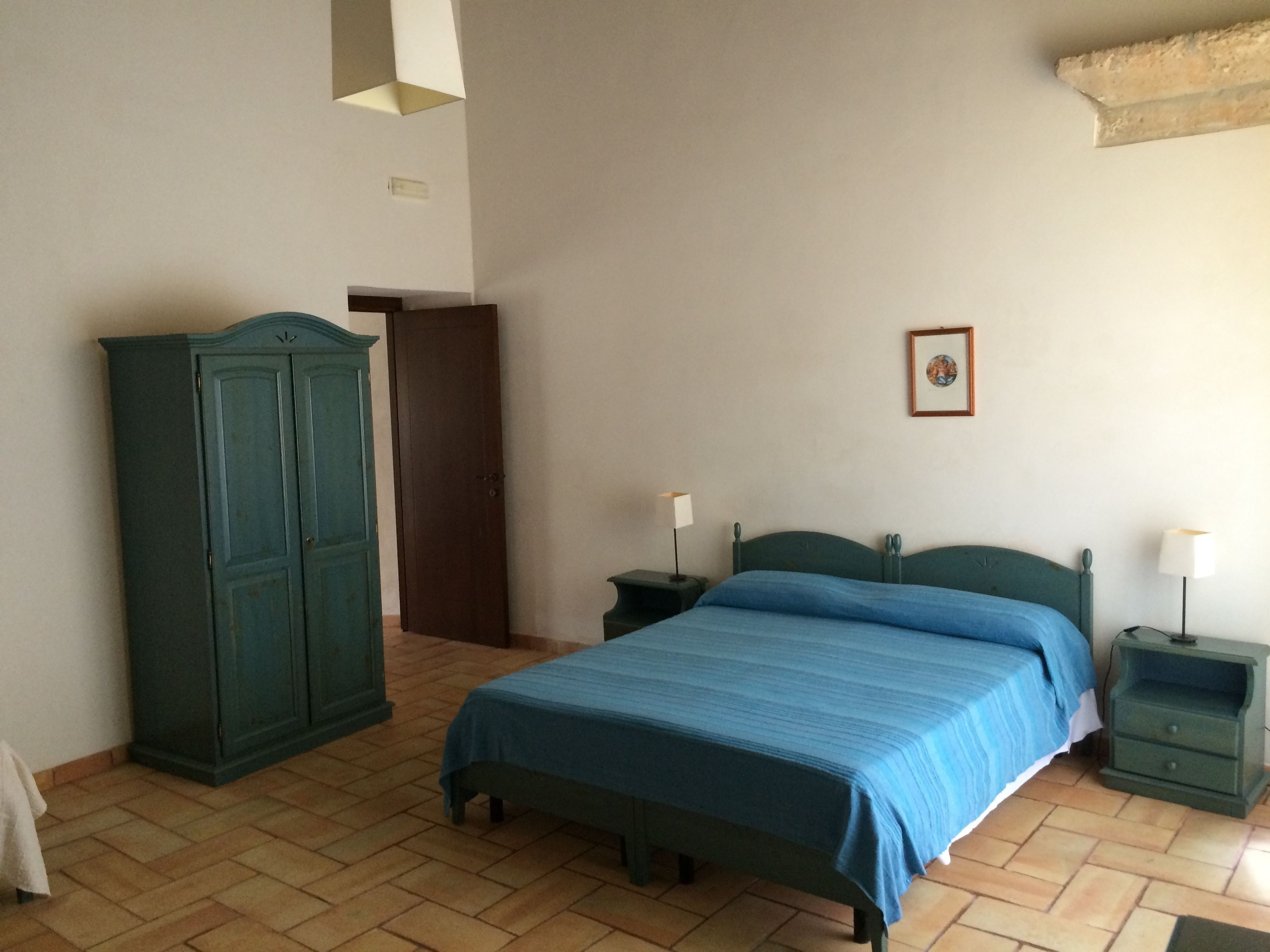 Een slaapkamer met een bed, een kledingkast, een nachtkastje en een lijst aan de muur.