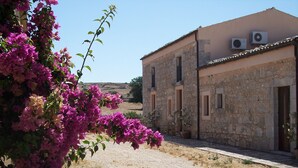 Ein Steinhaus mit einem Feldweg, umgeben von Bougainvillea-Blumen.