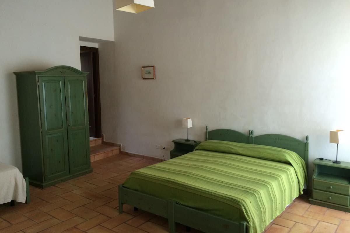 Quarto com cama verde, mesa de cabeceira, penteadeira e porta que dá para outro cômodo.