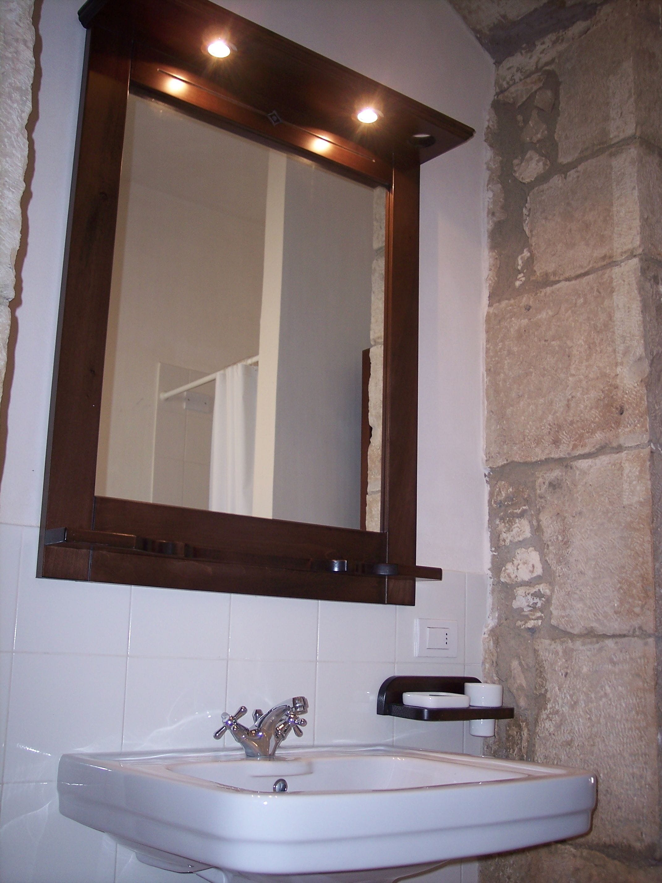 A bathroom with a white sink, a wooden-framed mirror, and a stone wall.