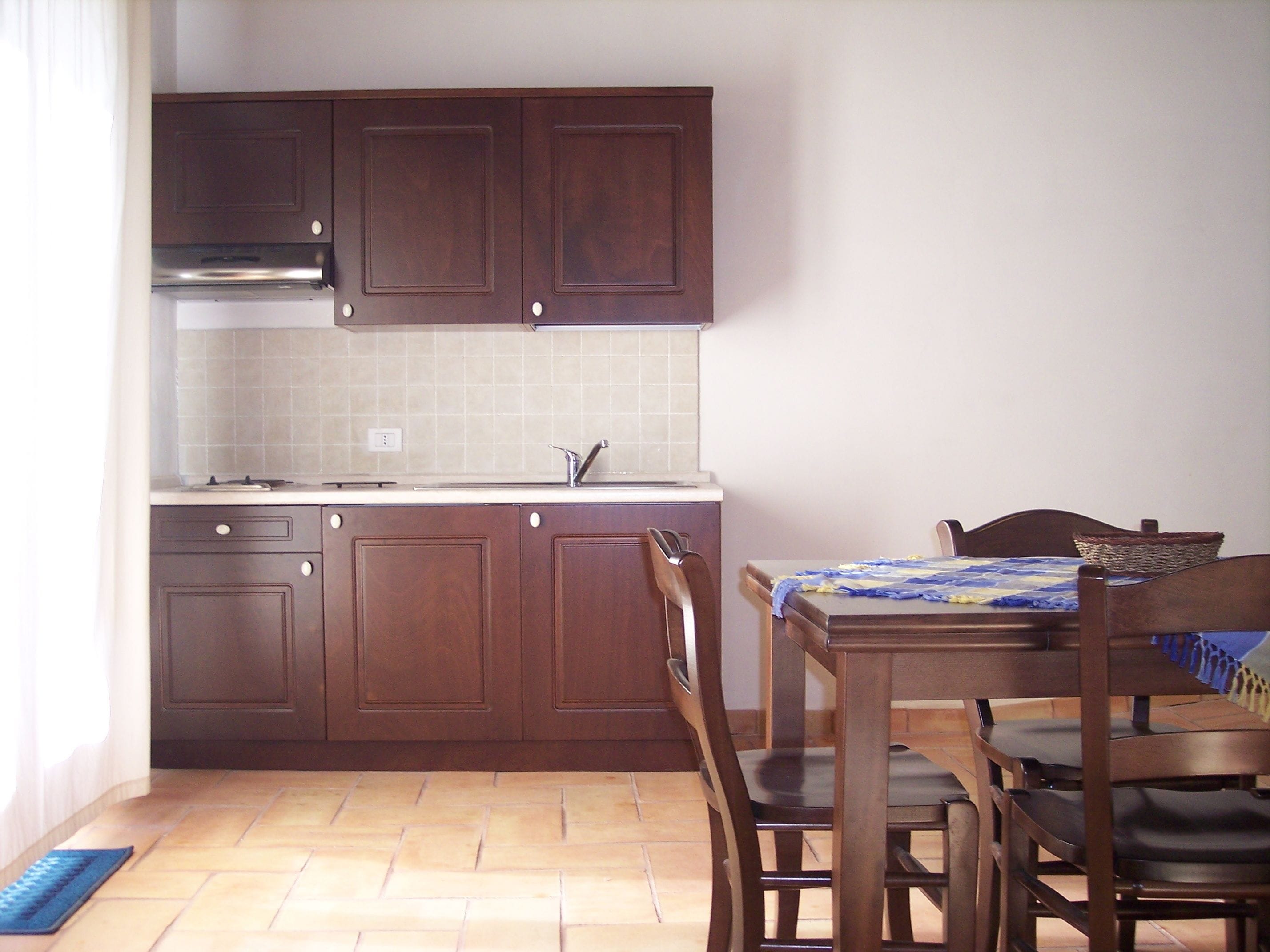 Una cocina compacta con armarios de madera, salpicadero de azulejos y una zona de comedor con mesa y sillas.